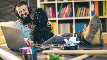 A man wearing headphones using a laptop with a dog on his lap. 