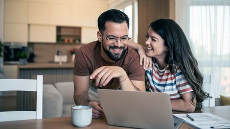 A smiling couple looking at a laptop.